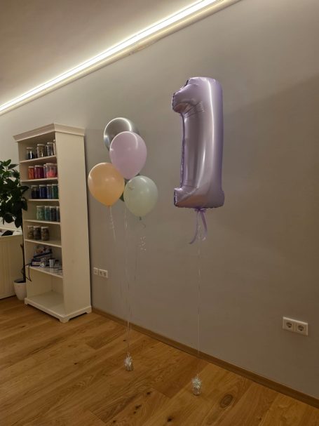 Schwebende Zahl & Ballon-Bouquet aus Latex-Luftballons Lila Luftballon in Form der Zahl 1 und mehrere bunte Ballons in einem Raum.