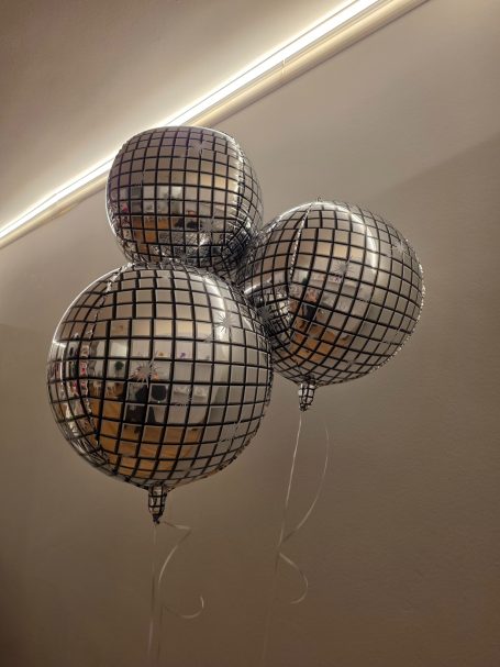 Discokugel Folienballons Drei silberne Ballons mit einem karierten Muster, schwebend an Schnüren.